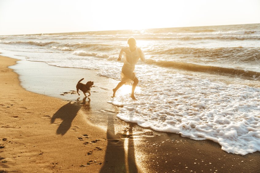 a person running across a beach next to the ocean with a dog