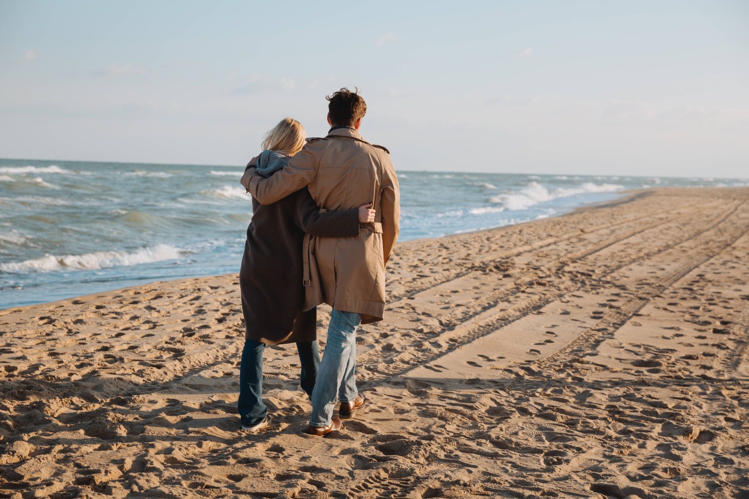 Couple walking on a sandy beach with waves in the background.