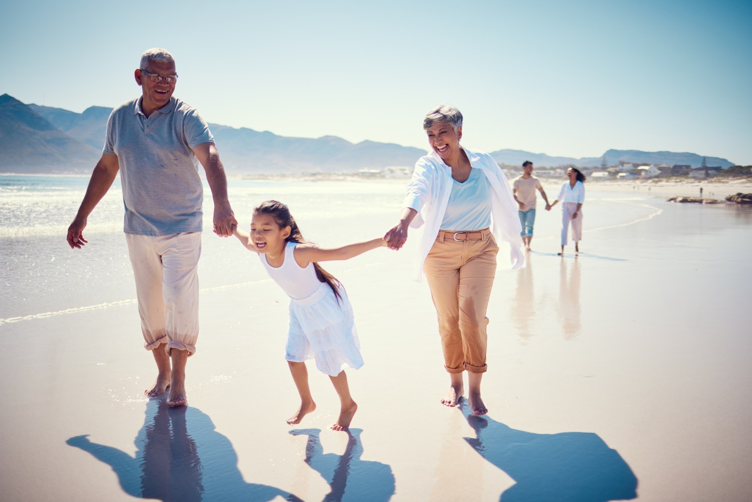 Beach, holding hands and playing, grandparents with girl, family walking on ocean sand together. Fun, vacation and happy senior man and woman with children bonding, quality time and summer in nature