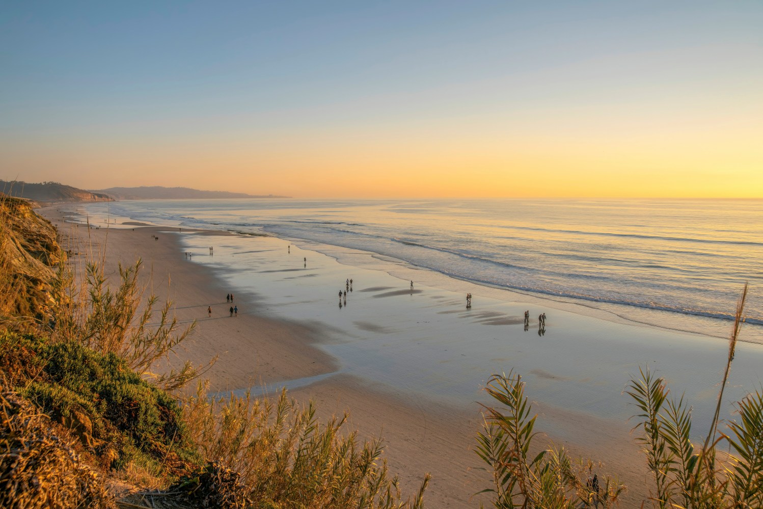Beach at sunset with people walking along the shoreline.