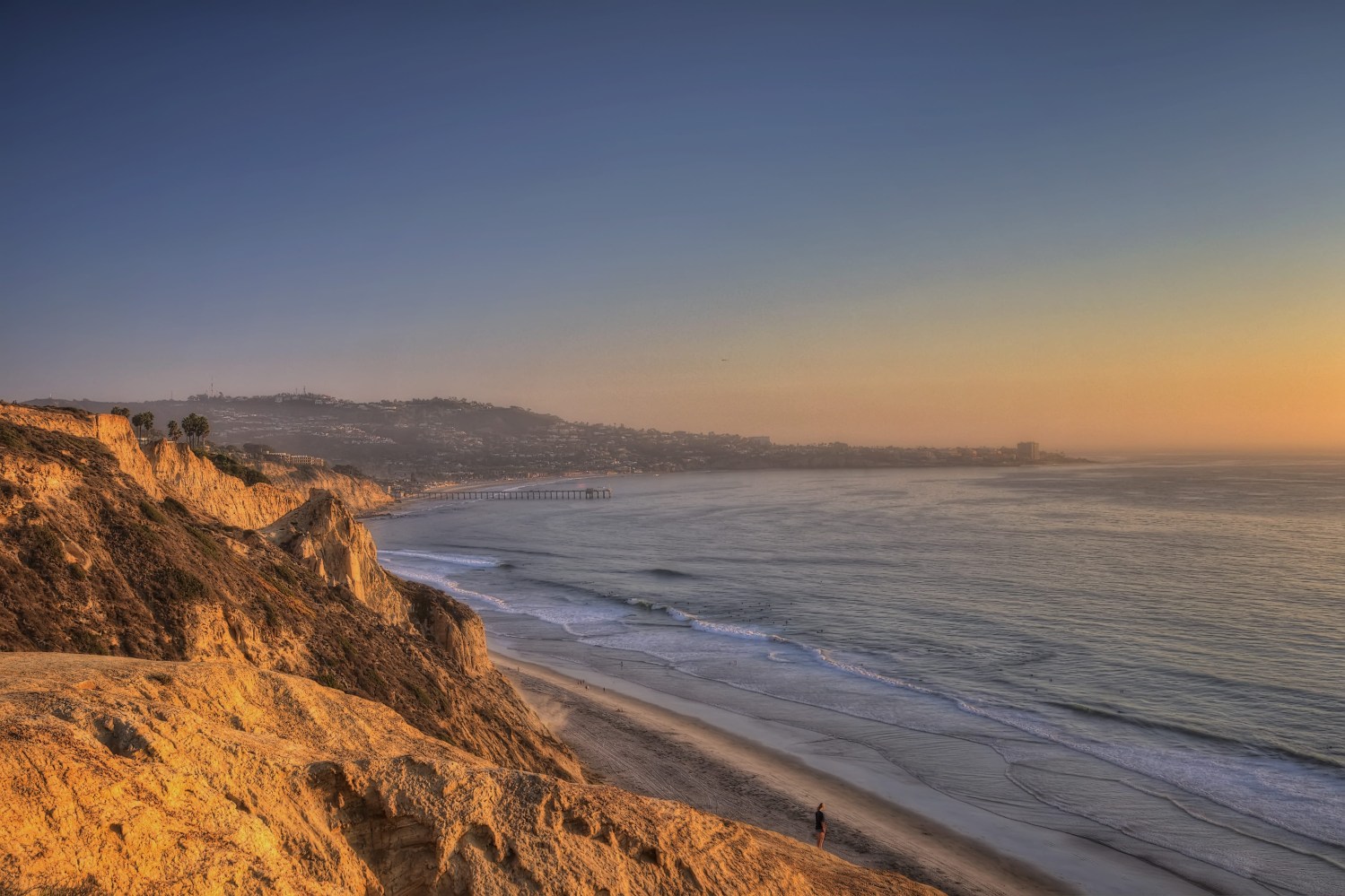 Del Mar San Diego Cliffs overlooking a serene beach at sunset with distant pier and calm waves.