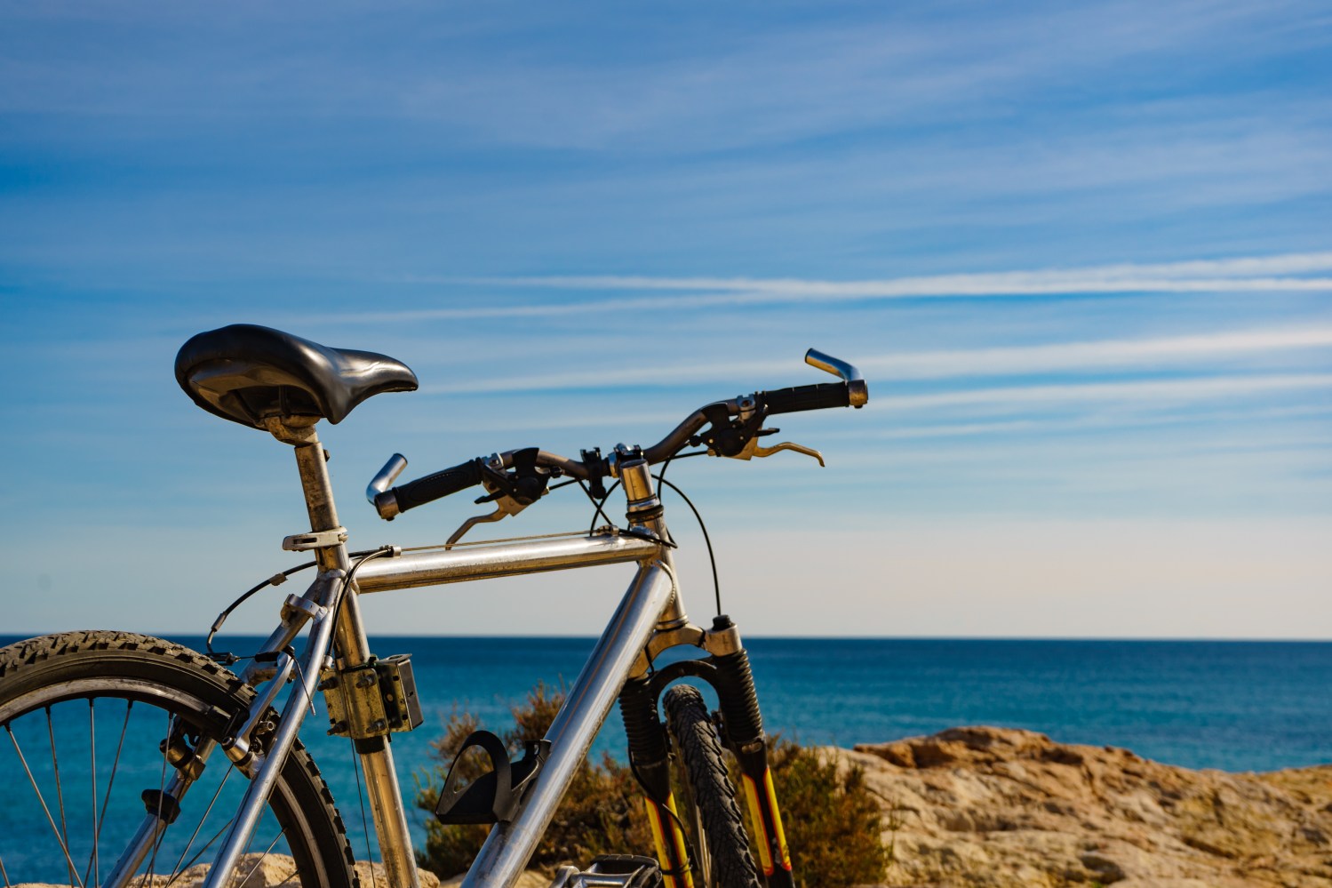 Bicycle parked on rocky cliff overlooking the ocean under a clear blue sky.