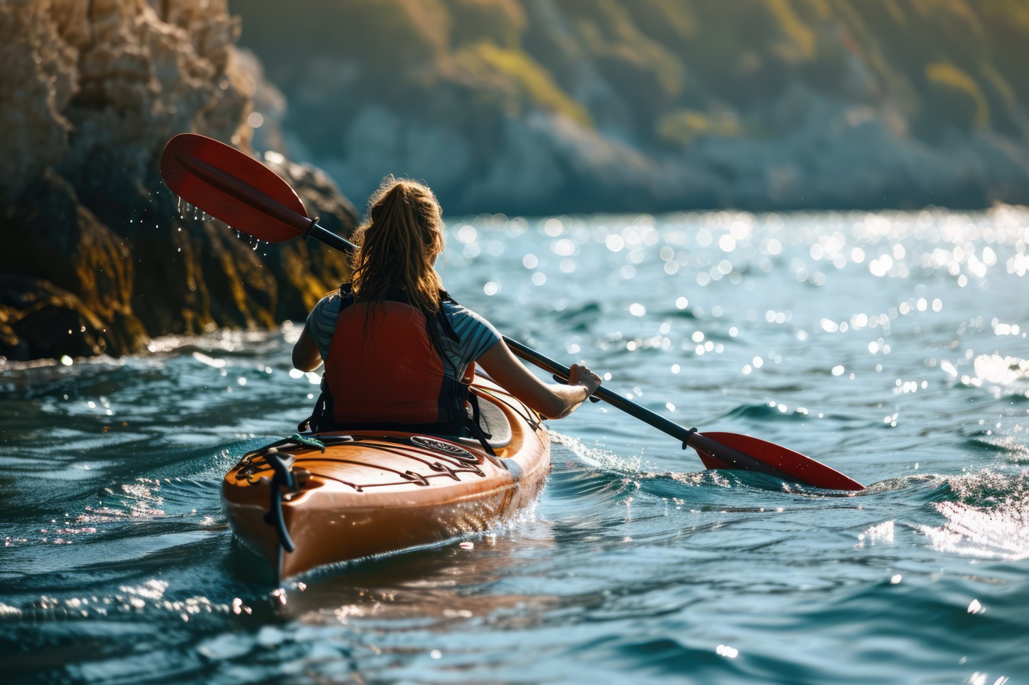 Woman kayaking on a sunny day near rocky coast, wearing a life jacket.