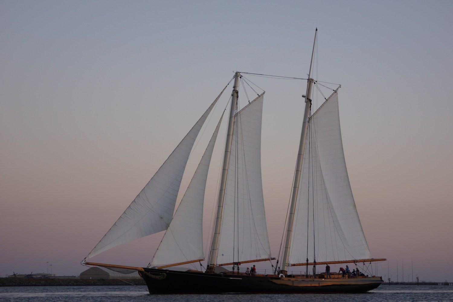 Sailing ship with large sails at sunset on calm water.