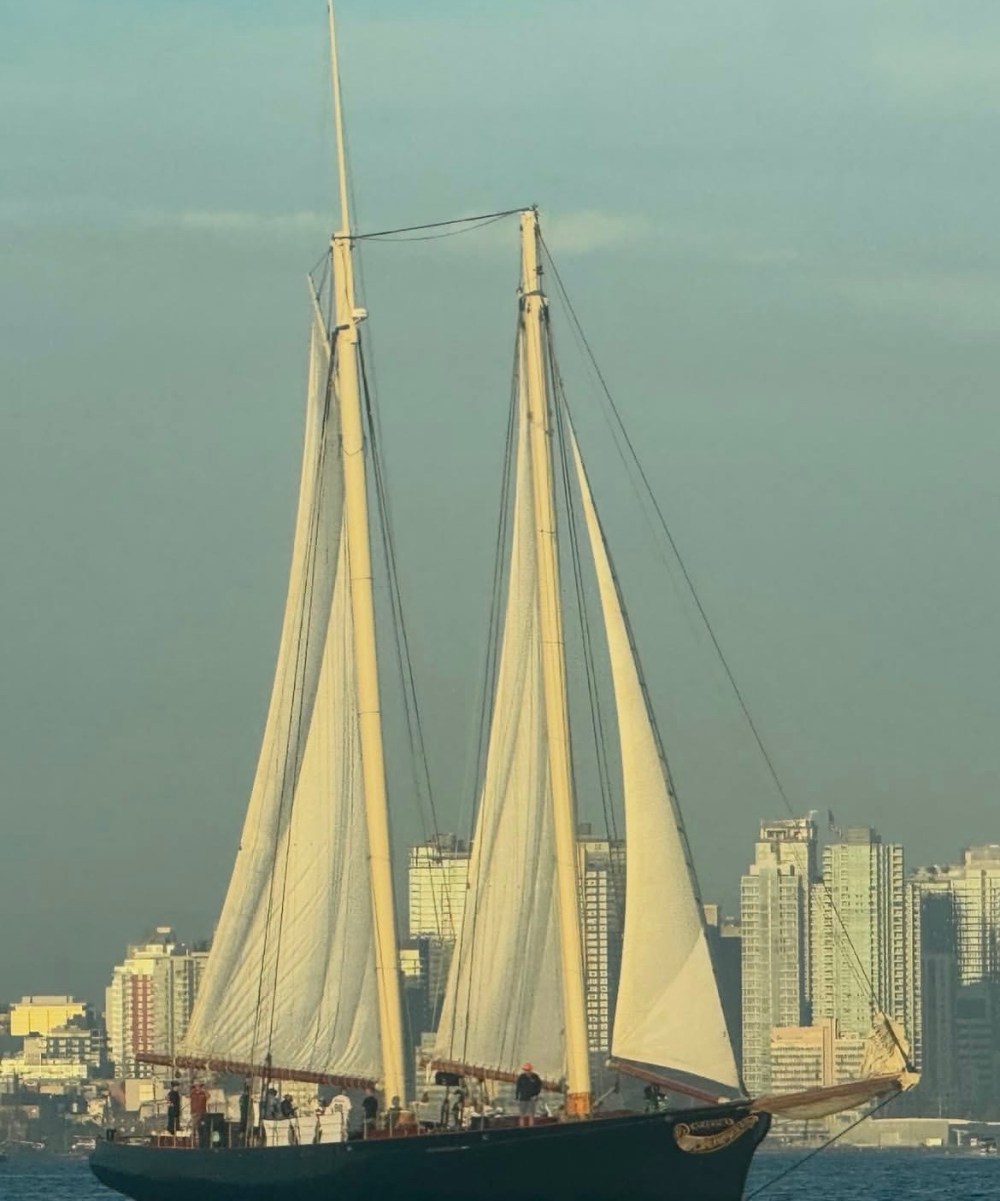 Tall ship with sails unfurled on a city skyline backdrop.