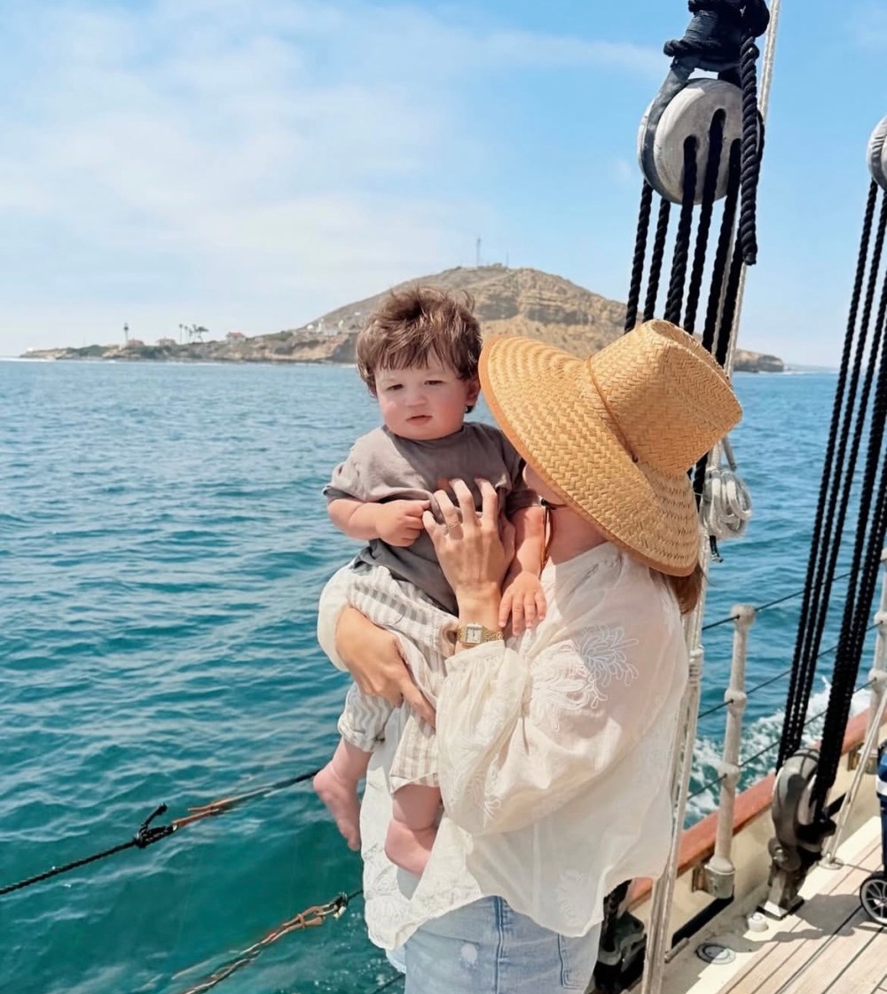 Woman in straw hat holds a child on a boat with island in background.