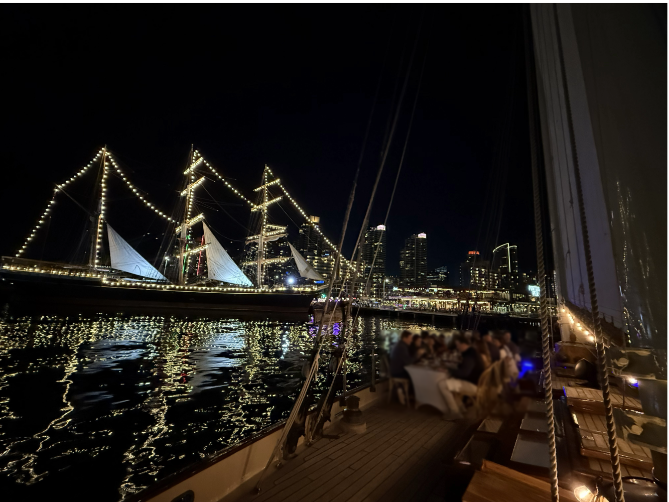 Night view of illuminated sailboat on water, city skyline in background.