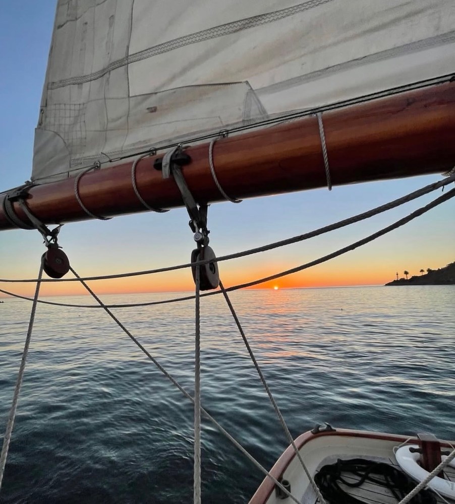 View of a sailboat mast at sunset over calm ocean waters.