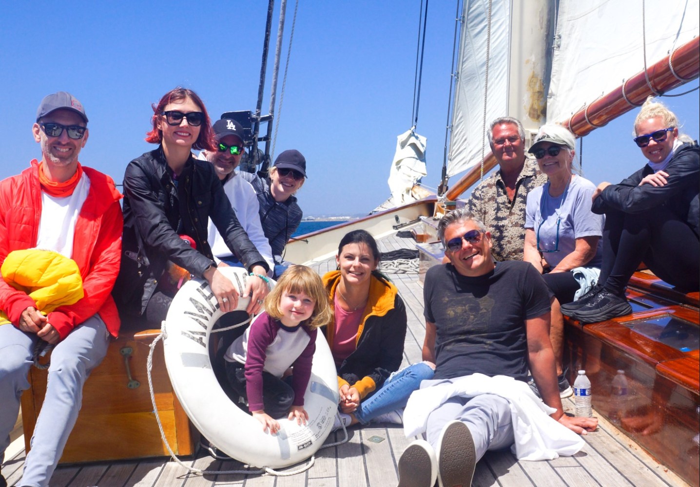 Group of people smiling on a sailboat under clear blue sky.